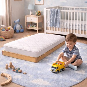 May include: A child's bedroom with a crib, a low wooden bed frame with a white mattress, and a blue rug. The room is decorated with hot air balloon and cloud wall decals. A child is playing with a yellow toy truck.