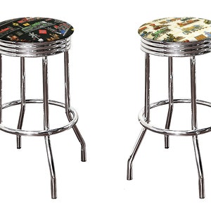 May include: Two chrome bar stools with patterned seat cushions. The seat cushions feature a black and white design with a variety of images, and a cream and brown design with a variety of images.