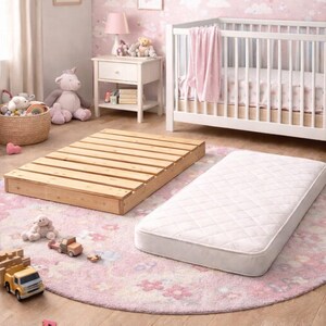 May include: A nursery scene with a white crib, a wooden bed frame, and a white mattress. The room has pink walls with rainbow and cloud patterns, a pink rug, and various toys.