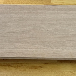 May include: A rectangular wooden tabletop with rounded corners. The light-colored wood grain runs horizontally across the surface. The tabletop is a light brown color and appears to be unfinished.