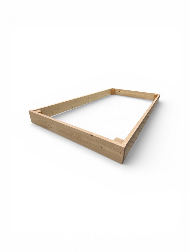 May include: A rectangular wooden frame, constructed from light-colored lumber, is presented against a white background. The frame is assembled with corner joints, showcasing the natural wood grain and texture. The design suggests a base or support structure.