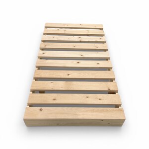 May include: A light-colored wooden pallet with evenly spaced horizontal slats. The pallet is made of unfinished wood and is rectangular in shape. The design is simple and functional, suitable for various uses.