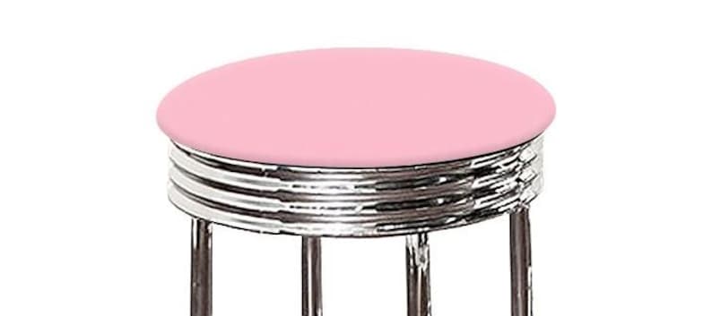 May include: A retro-style stool with a round, light pink seat. The seat is supported by a chrome-plated, multi-ringed base and four chrome legs. The stool has a classic diner or soda shop aesthetic.