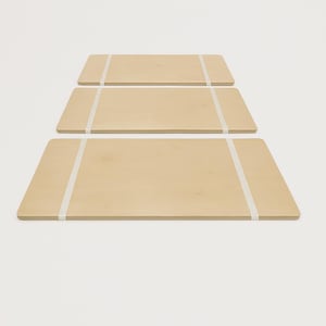 May include: Three light-colored wooden serving trays with rounded corners are stacked. Each tray is secured with a white band. The trays are arranged in a descending order, with the largest tray at the bottom.