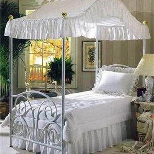 Pu&ograve; includere: Una struttura per letto a baldacchino in metallo bianco con testiera e pediera a volute. Il letto &egrave; coperto da un piumino trapuntato bianco, una balza coordinata e un singolo cuscino bianco con bordo arricciato, sormontato da un baldacchino.