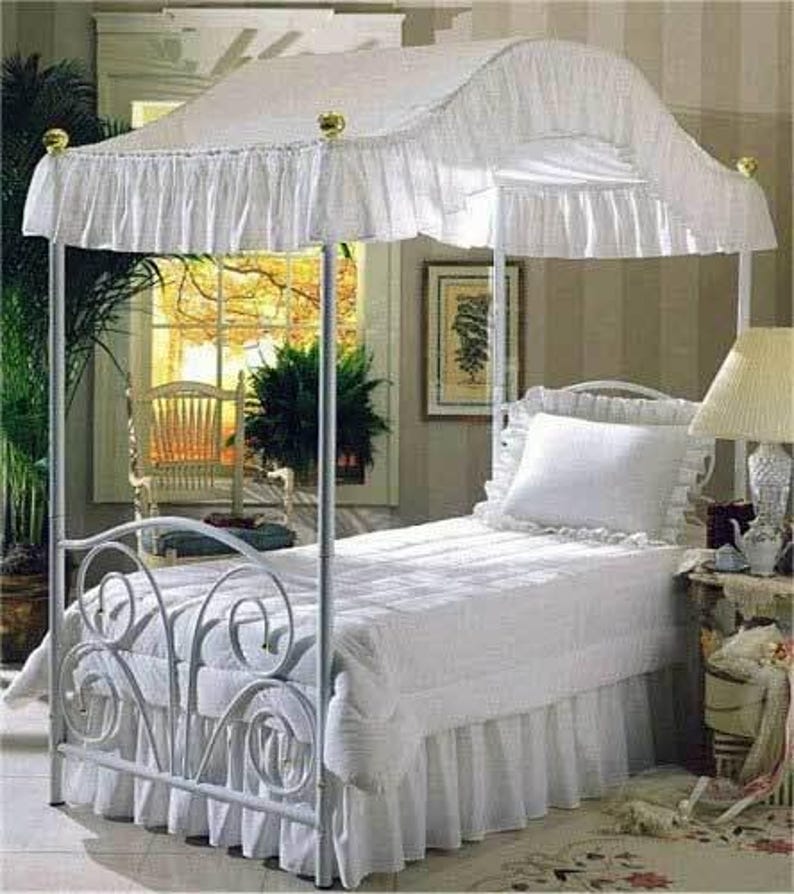 Pu&ograve; includere: Una struttura per letto a baldacchino in metallo bianco con testiera e pediera a volute. Il letto &egrave; coperto da un piumino trapuntato bianco, una balza coordinata e un singolo cuscino bianco con bordo arricciato, sormontato da un baldacchino.