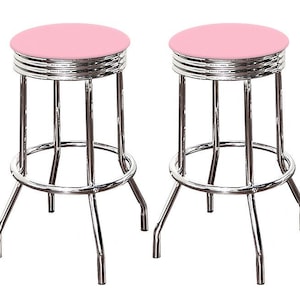 May include: Two retro-style bar stools. Each stool has a round, light pink seat and a chrome-finished metal frame. The frame features a footrest and four legs. The seats are approximately 12 inches in diameter.