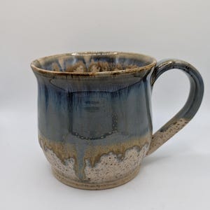May include: Handmade ceramic mug with a unique glaze. The mug features a dark blue and brown glaze that drips down the sides, creating a textured effect. The handle is a matching colour. A perfect addition to any kitchen.
