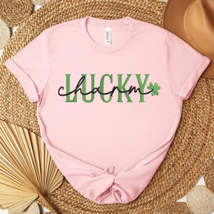 May include: Pink t-shirt with the text "Lucky charm" in green letters with a green four-leaf clover graphic.