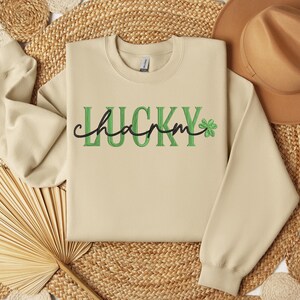 May include: A beige sweatshirt with the text "LUCKY charm" in green and black lettering with a green four-leaf clover.