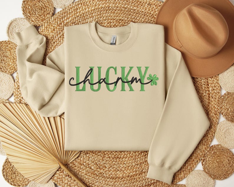 May include: A beige sweatshirt with the text "LUCKY charm" in green and black lettering with a green four-leaf clover.