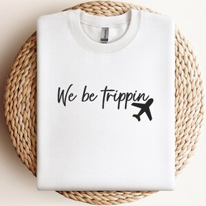 May include: White sweatshirt with black text that reads "We be trippin'" and a small airplane graphic.