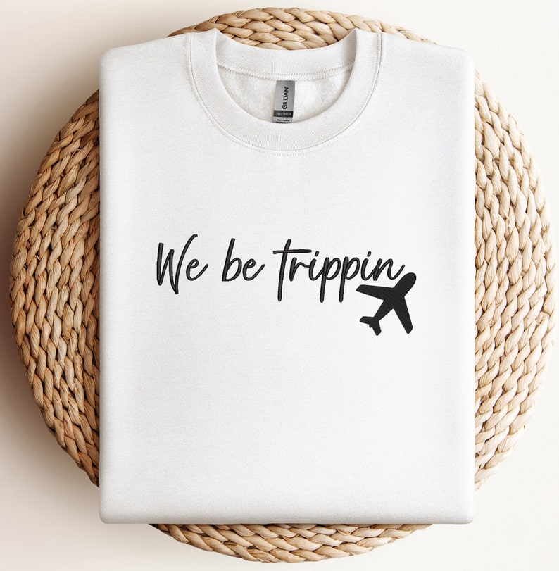 May include: White sweatshirt with black text that reads "We be trippin'" and a small airplane graphic.