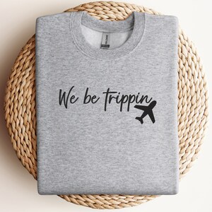May include: Gray sweatshirt with the text "We be trippin'" and a black airplane graphic.