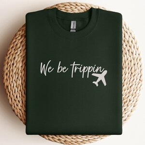 May include: A dark green sweatshirt with the text "We be trippin'" in white lettering and a white airplane graphic.