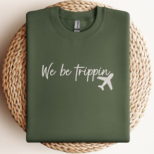 May include: A green sweatshirt with the text "We be trippin'" in white lettering and a white airplane graphic.