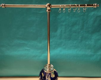 May include: A silver jewelry stand with a blue and white glass base. The stand has a horizontal bar with several rings attached.