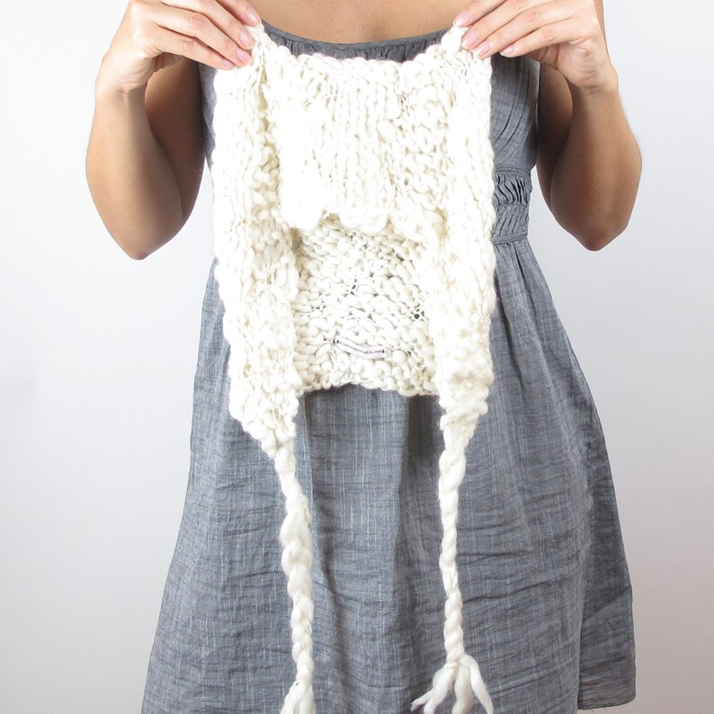 May include: A white knitted cowl with long, braided ties. The cowl is made of a chunky yarn and has a loose, drapey fit.