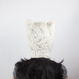 May include: White knitted hat with ear flaps. The hat is made of a soft, fluffy yarn and has a loose, slouchy fit.
