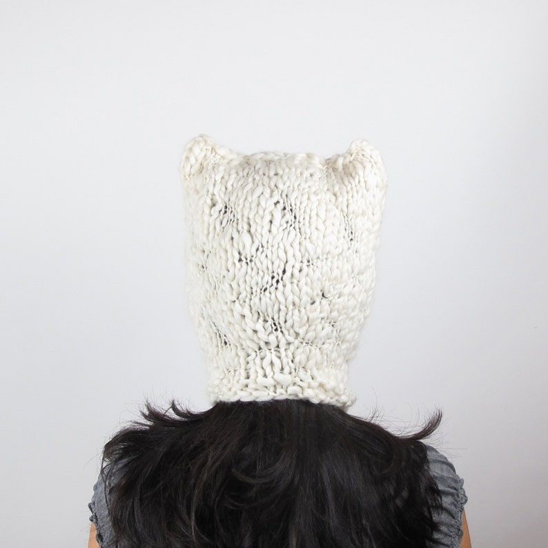 May include: White knitted hat with ear flaps. The hat is made of a soft, fluffy yarn and has a loose, slouchy fit.