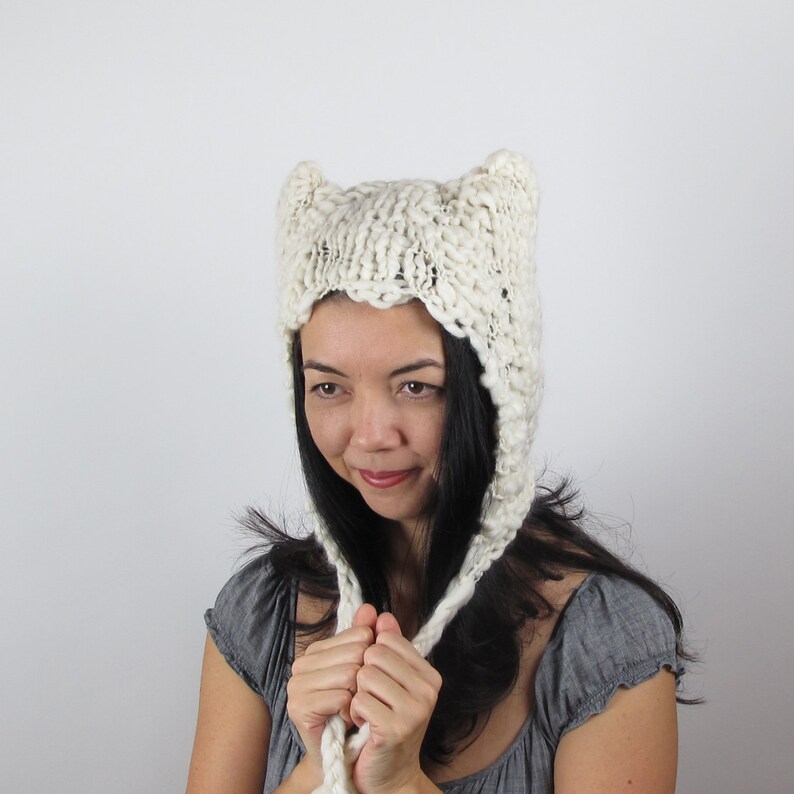 May include: A white knitted hat with cat ears. The hat is made of a chunky yarn and has a loose, slouchy fit.
