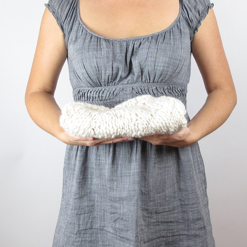 May include: A person holding a white knitted blanket in front of their chest. The blanket is folded in half and the person is holding it with both hands.
