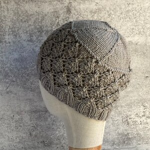 May include: A gray knitted hat with a textured pattern. The hat is on a white mannequin head.
