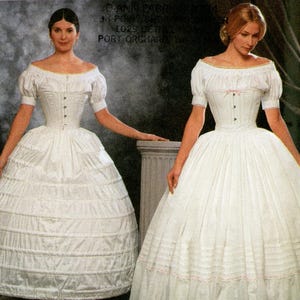 May include: A Simplicity sewing pattern envelope 9764 for The Fashion Historian by Martha McCain. The cover displays two white off-the-shoulder dresses with puffed sleeves, fitted bodices, and full skirts. One dress features horizontal tucks and lace trim.