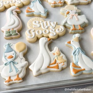 May include: Assortment of decorated sugar cookies featuring goose designs. Cookies include geese with hats, bows, and boots, and the phrase "Our Little Silly Goose". The cookies are decorated with white, blue, orange, and yellow icing.