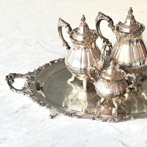 May include: A silver tea set with a teapot, creamer, and sugar bowl on a silver tray with ornate handles.