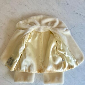 May include: Cream-colored faux fur coat with a hood and satin lining. The coat has a classic design with a soft, plush exterior and a smooth, light yellow interior. The coat has a label that reads "BORG".
