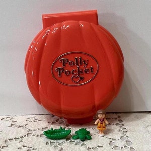 May include: A bright orange Polly Pocket compact with a heart logo. The compact is open and shows a small doll, a green turtle, and a green boat.