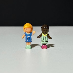 May include: Two plastic dolls, one with blonde hair and a blue dress, the other with brown skin and a green dress.