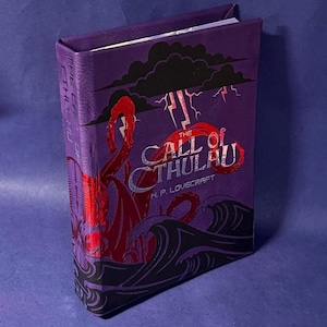 May include: A purple hardcover book titled "The Call of Cthulhu" by H.P. Lovecraft. The cover features a red illustration of a creature, black waves, and lightning bolts against a dark cloud. The book's spine also displays the title.