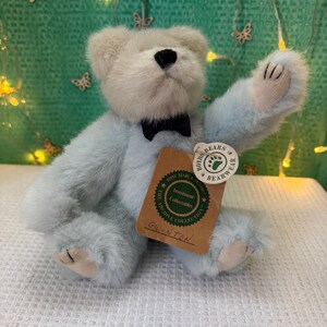 May include: A light blue Boyd's Bears plush bear named Gwinton, wearing a black bow tie. The bear has a cream-colored head and paws, and a tag that reads "The Archive Collection". The bear is sitting on a white surface.