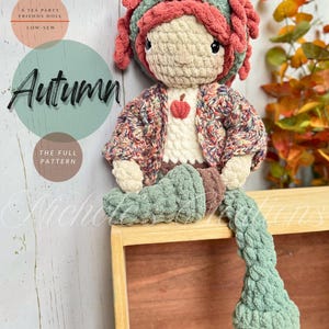 May include: A crocheted doll named Autumn with textured red hair, a green headband, and a multi-colored cardigan over a cream-colored top with a small red apple appliqué. The doll has green legs and brown feet, with text reading A TEA PARTY FRIENDS DOLL, LOW-SEW, Autumn, THE FULL PATTERN, and Nichole's Creations.