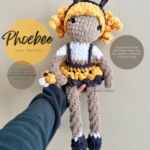 May include: A handmade crochet doll named Phoebee, featuring a bee-themed design. The doll has a yellow and black skirt, a white top, and a yellow headpiece with antennae. The text "Phoebee and Friend" is visible.