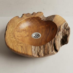 Könnte beinhalten: Ein handgefertigtes Waschbecken aus Holz mit einer natürlichen, organischen Form. Das Waschbecken besteht aus hellbraunem Holz mit sichtbarer Maserung und einem Edelstahl-Abfluss. Die Kanten des Waschbeckens haben eine raue, unfertige Textur.