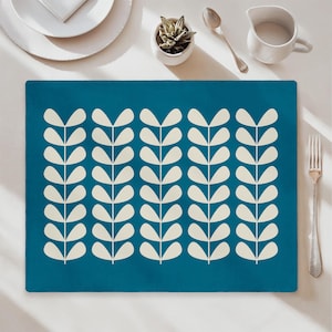 May include: Teal placemat featuring a repeating pattern of cream-coloured leaf-like shapes. The rectangular placemat is on a white surface, with a fork, spoon, and small succulent plant in the background. A minimalist design for dining.