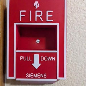 May include: A red fire alarm pull station with white lettering and a white border. The word "FIRE" is at the top, with "PULL DOWN" and an arrow in the middle. The brand name "SIEMENS" is at the bottom.