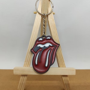 May include: A red and white tongue keyring with a black outline. The keyring is hanging from a silver chain on a wooden easel.
