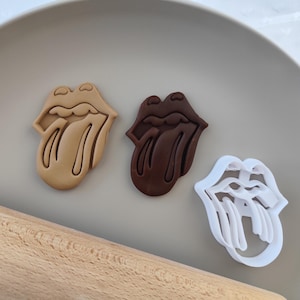 Puede incluir: Tres cortadores de galletas con forma de lengua con labios, uno es marrón, otro beige y otro blanco.