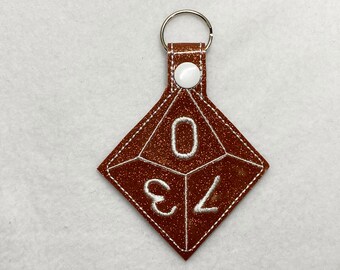 May include: A brown glitter keychain shaped like a D6 dice with white stitching and the numbers 0, 3, and 4.