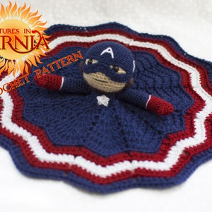 May include: A crocheted baby blanket in red, white, and blue with a crocheted Captain America doll attached. The blanket has a scalloped edge and the doll has a red, white, and blue costume with a star on the chest.