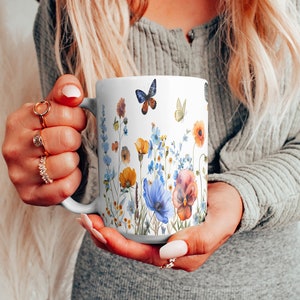 May include: White ceramic mug with a floral design featuring blue, yellow, and orange flowers, green leaves, and butterflies. The mug has a handle on the right side.