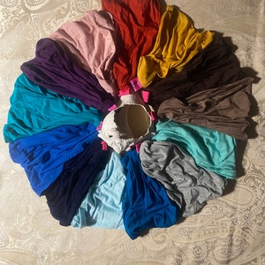 May include: A collection of 12 fabric headbands in various colors, including teal, purple, pink, red, yellow, brown, blue, and gray. The headbands are arranged in a circle on a patterned fabric background.