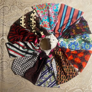 May include: A collection of colorful headbands arranged in a circular pattern around a white, textured vase. The headbands display various patterns, including stripes, polka dots, geometric shapes, and floral designs. The color palette includes red, blue, pink, and brown.