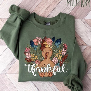May include: A green sweatshirt with a Thanksgiving turkey design and the word "thankful" printed on the front. The turkey is surrounded by flowers and leaves.