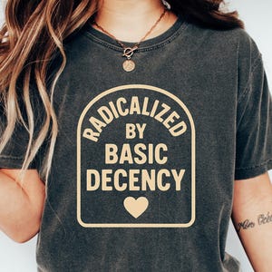 May include: A dark gray t-shirt with a yellow graphic that reads "Radicalized by Basic Decency" with a heart symbol.