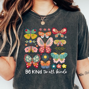 May include: A dark gray t-shirt with a colorful butterfly design and the text "Be Kind to all kinds".